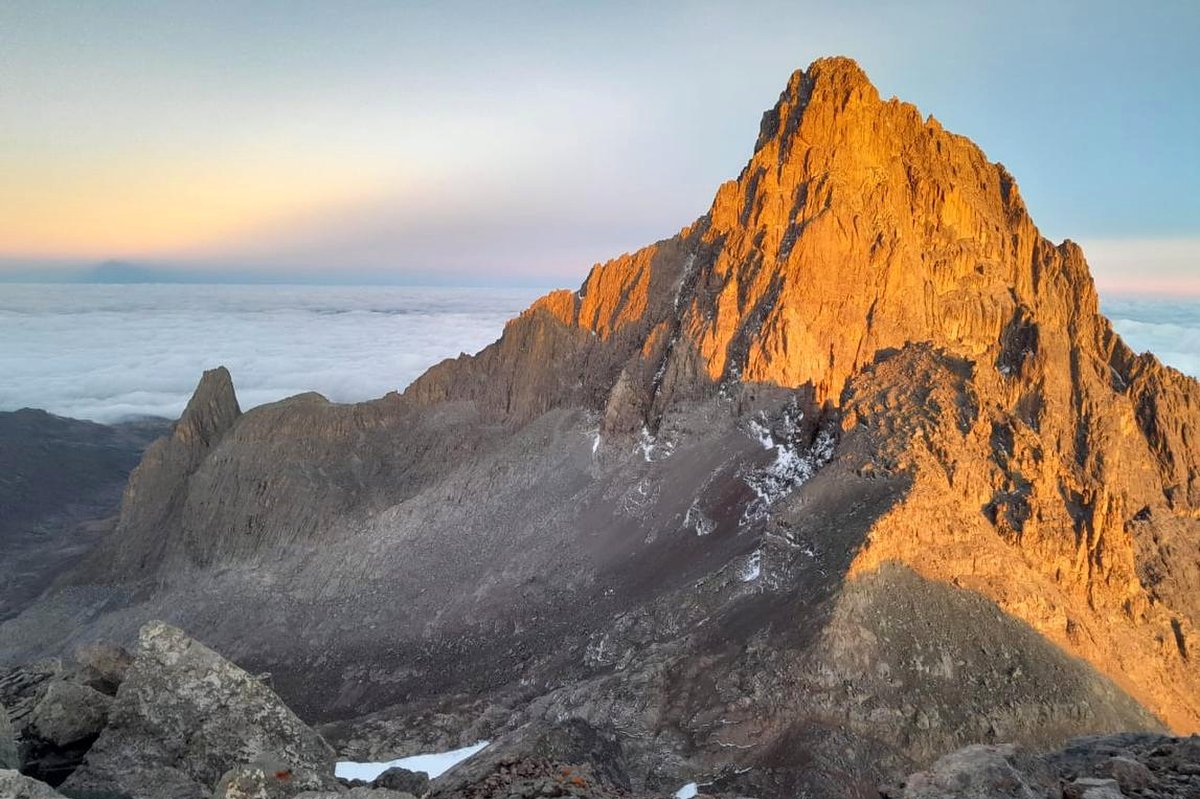 Gyllene soluppgång som lyser upp en karg bergstopp som reser sig över ett hav av moln, med stenig förgrund