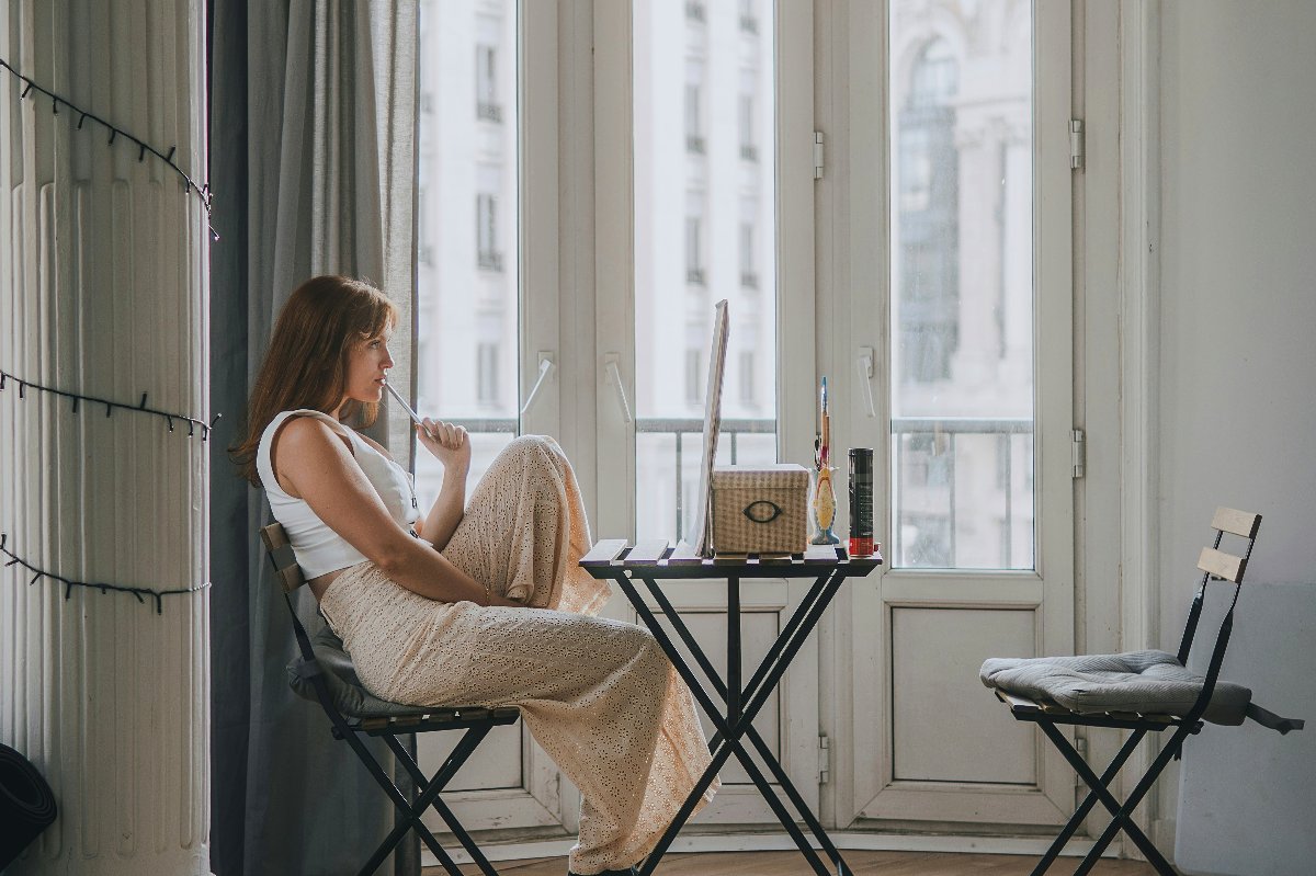 Donna seduta pensierosa vicino ad alte finestre cittadine a un piccolo tavolo con taccuino e caffè — La flessibilità conta più di quanto pensi