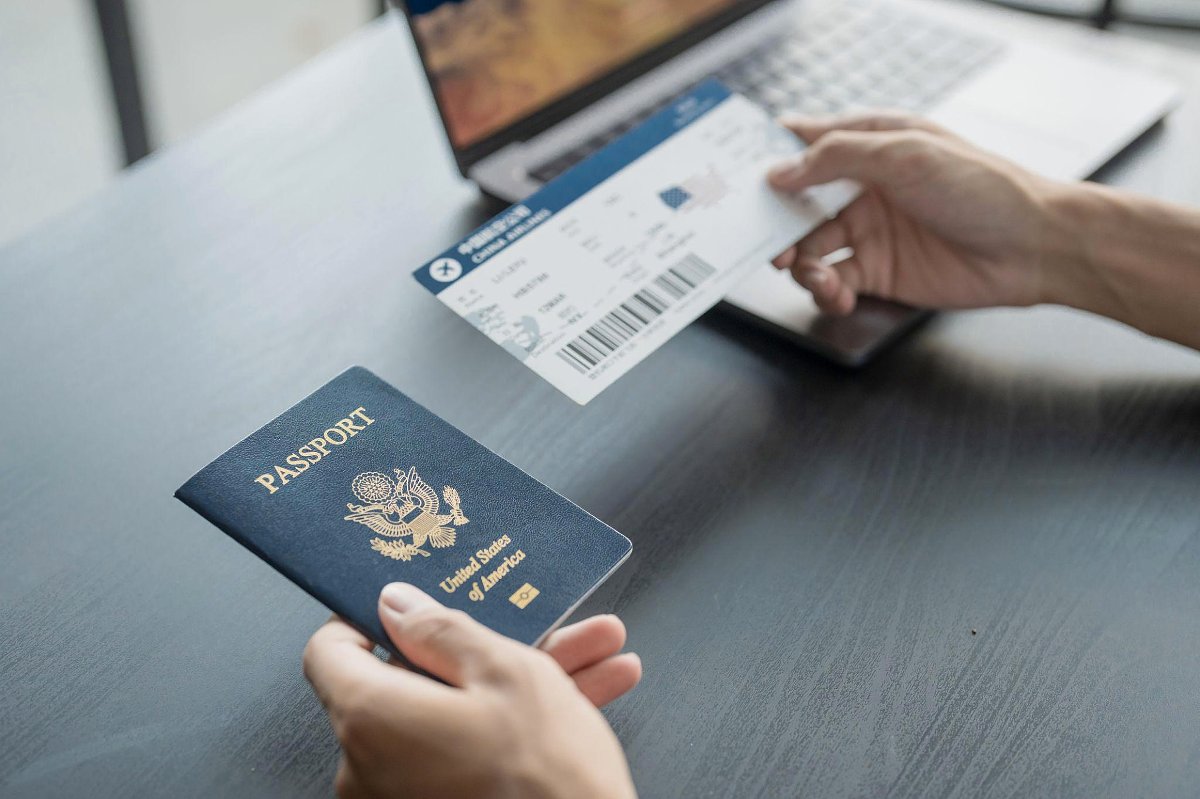 Blog di Niroskos 'Da dove cominciare...': passaporto USA e carta d'imbarco su una scrivania, mano che tiene il biglietto accanto a un portatile