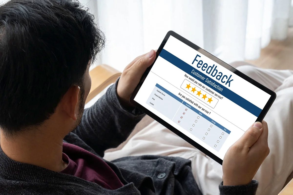 Veduta oltre la spalla di una persona che tiene un tablet con un sondaggio di feedback clienti e una valutazione a cinque stelle — immagine del blog: 'Le recensioni raccontano storie che la pubblicità non racconterà mai'
